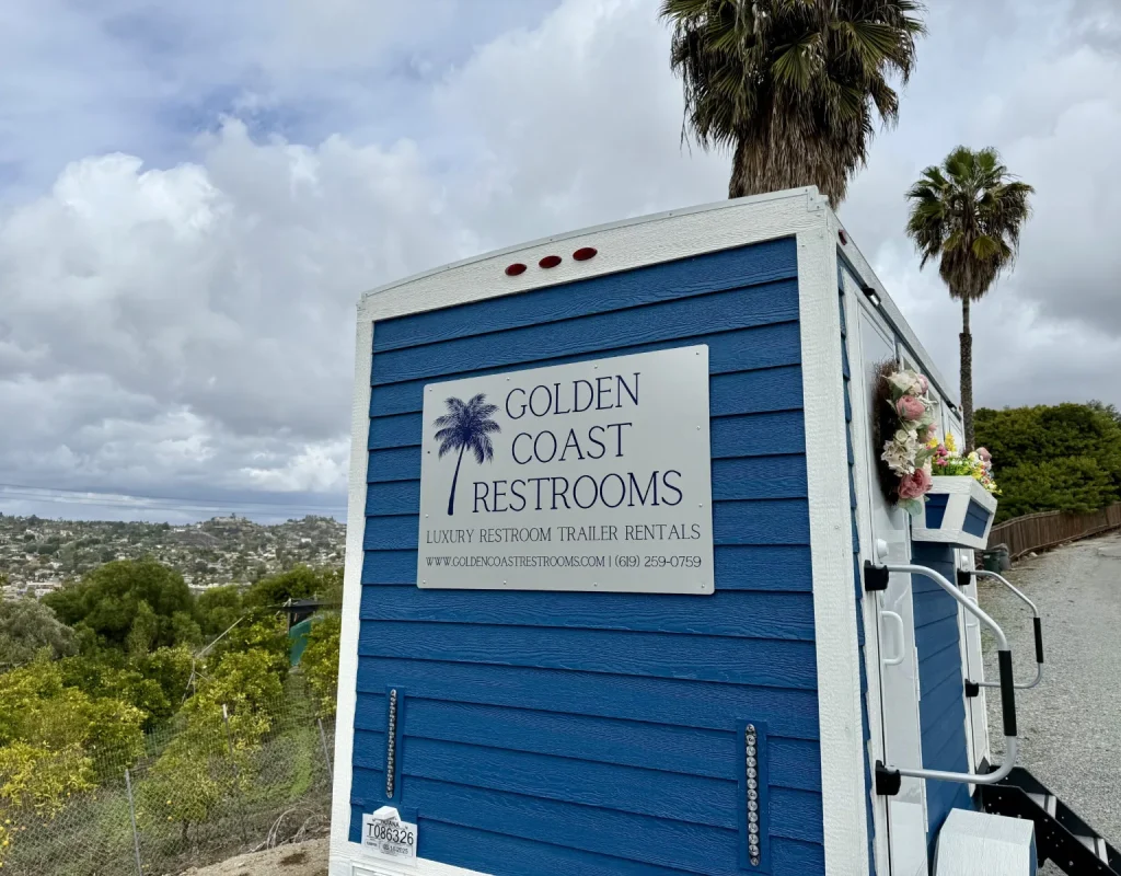 Side of a blue Golden Coast Restrooms luxury restroom trailer showing the company sign, delivered and set up for an event in Escondido, CA.