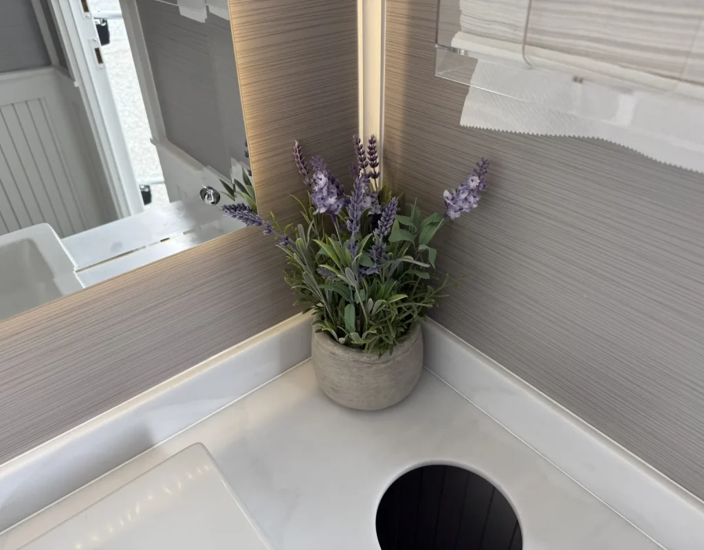 Restroom trailer interior with a white sink, faucet, and a vase of fresh flowers on the counter, prepared for an event rental in San Diego, CA.